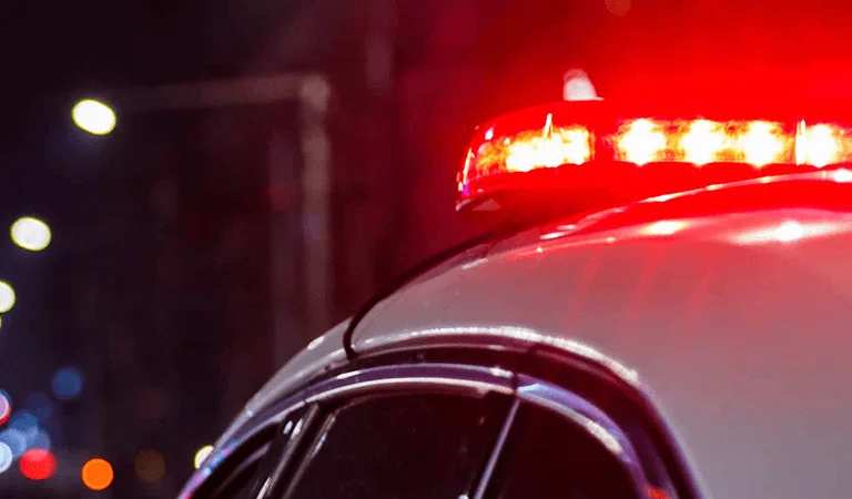 A red and white police car with its emergency lights activated, standing by on a city road.