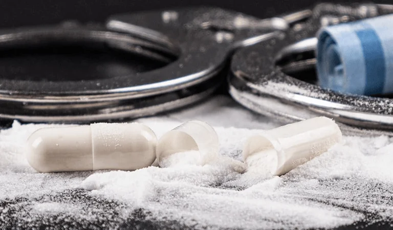 An image featuring scattered white powder next to opened capsules and metallic handcuffs, suggesting a criminal or drug-related theme.