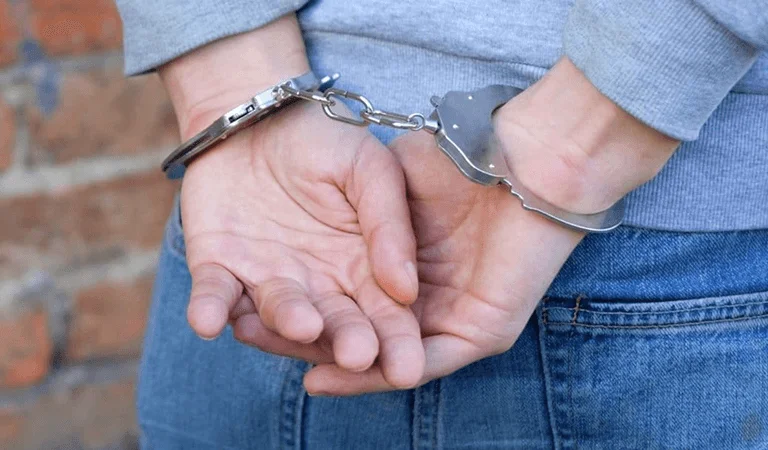 A close-up of a person's hands restrained by handcuffs, suggesting a legal situation.