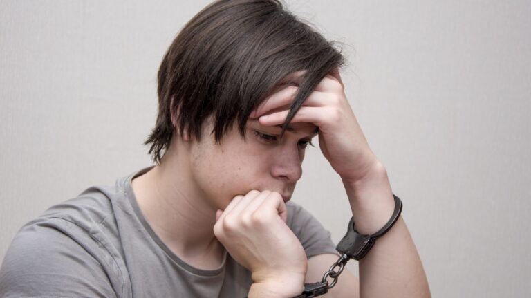 A handcuffed teenager sits on a grey background